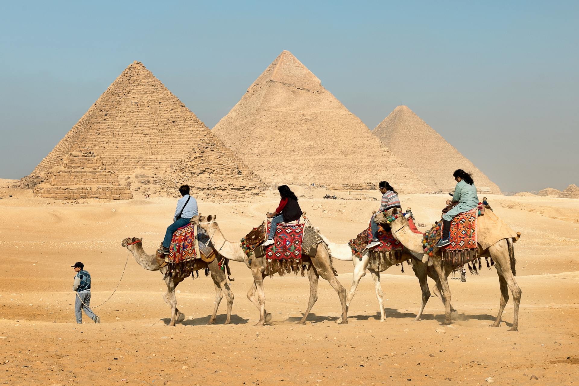 tour of four people on a camel with background of three pyramids in Egypt